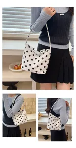 Detail view of a chic white and black polka dot shoulder bag worn by a model indoors.