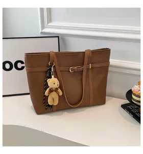 Close-up detail view of a brown PU leather tote shoulder bag featuring a cute plush bear charm.