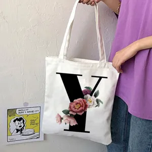 Primo piano della borsa tote in tela bianca con una grande lettera Y nera audace e stampa floreale.