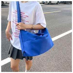 Detail shot of the large blue canvas crossbody shoulder bag, showcasing outdoor wearing style.
