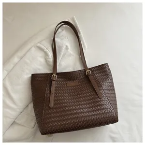 Detalle de bolso tote tejido en piel marron oscuro con asas dobles y hebillas metalicas.