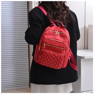 Detail shot of a red stylish quilted backpack with metallic studs and multiple zipper pockets.