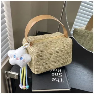Detailed view of the woven straw lunch box bag with cute plush cloud charm and handle.