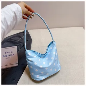 Detail shot of light blue shoulder bag with white polka dots, soft fabric and slim strap texture.