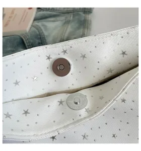 Detail view of white canvas star print shoulder bag magnetic snap hardware and fabric texture.
