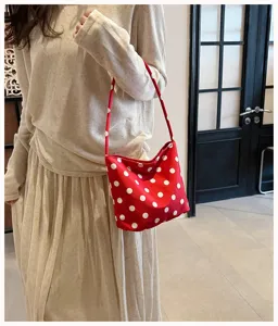 Detail shot of a stylish red polka dot shoulder bag carried by a model in beige outfit.