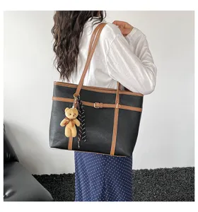 Detail shot of black leather tote bag with brown straps, buckle accent and cute bear charm.