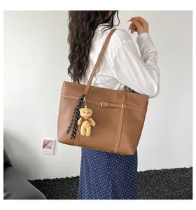Detail view of the brown leather tote bag with cute bear pendant worn on shoulder.