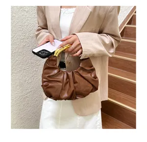Detailansicht einer stilvollen braunen gerafften Handtasche mit goldenem Metallgriff.