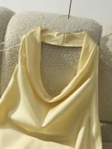Dettaglio top in raso giallo con collo halter, design smanicato drappeggiato per donna.