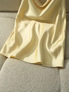 Primo piano dettagliato del top in raso giallo, texture liscia ed elegante drappeggio.