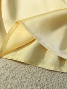Dettaglio di tessuto satinato giallo chiaro, trama drappeggiata liscia, cuciture fini, elegante.