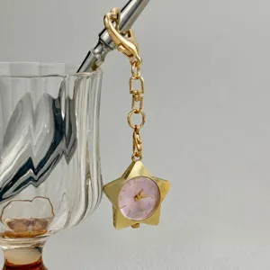 Detailansicht einer goldenen Stern-Taschenuhr als Schlüsselanhänger mit rosa Zifferblatt.