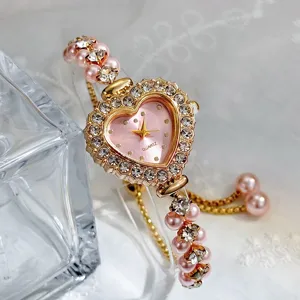 Nahaufnahme einer rosa Herz Quarz Uhr mit Strasssteinen und Perlen Armband Details.