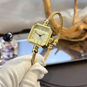 Detailansicht einer goldfarbenen Quarzuhr mit quadratischem Zifferblatt und gedrehtem Armreif.