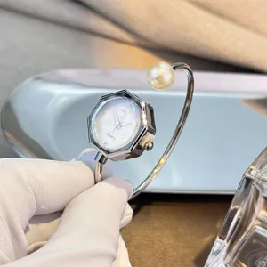 Vista detallada de un reloj brazalete hexagonal minimalista con un elegante adorno de perla fina.