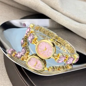 Goldfarbene Quarzuhr Detail, rosa Zifferblatt und funkelnde rosa Herz Kristallglieder.