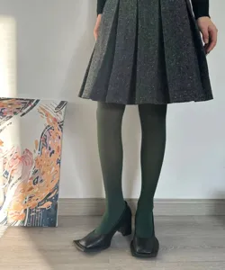 Close-up detail view of dark green velvet pantyhose paired with a stylish pleated skirt.