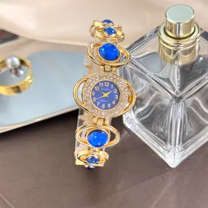 Close-up detail of women's gold-tone luxury stone bracelet watch with blue dial.