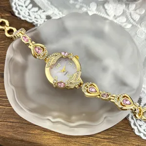 Detalle de reloj de cuarzo para mujer con correa dorada y piedras de cristal rosa.