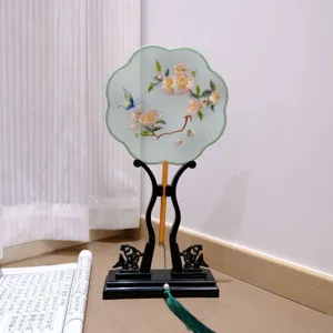 Detailed view of traditional Chinese embroidered round fan with wooden stand and green tassel.