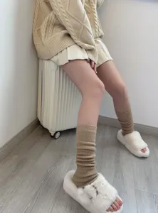 Detail view of cozy knit leg warmers in cream color paired with fluffy slippers indoors.