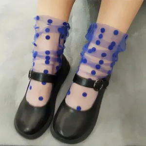 Close-up detail of sheer blue mesh socks with flocking polka dots paired with classic black shoes.