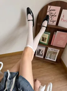 Detailed view of white hollow-out knit lace ruffle mid-tube socks paired with black shoes.