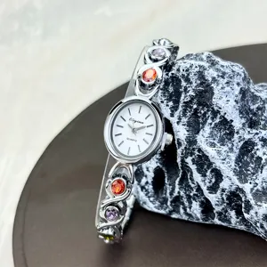 Detail view of the delicate oval quartz watch featuring colorful gemstone embedded band and white dial.