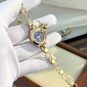 Detail shot of dainty gold heart-link bracelet quartz watch with dark blue dial and charm.