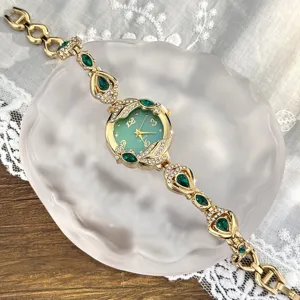 Detalle de reloj de cuarzo para mujer en tono dorado con gemas verdes y brillantes.