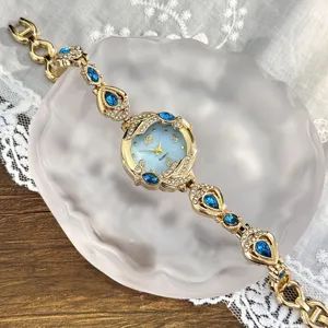 Reloj de cuarzo dorado para mujer con dijes de cristal azul y esfera de nácar detalle.