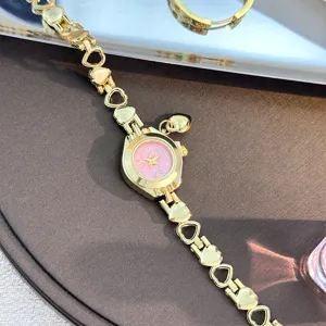Close-up detail of the gold heart-link quartz watch with pink dial and cute charm.