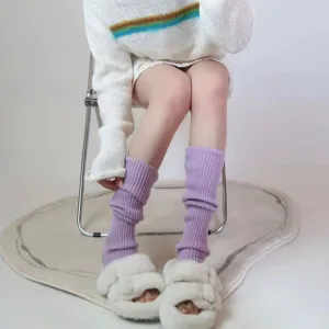 Detailed close-up view of stylish purple knit leg warmers and cozy white plush fuzzy slippers.