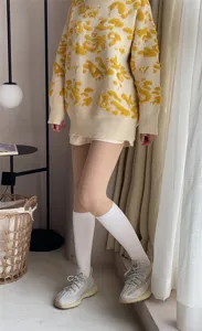 Stylish women's knit sweater with abstract pattern, paired with white socks and casual sneakers.