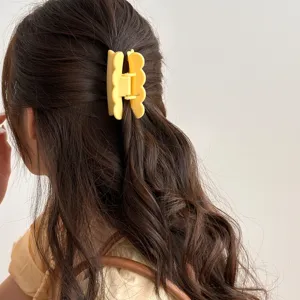 Gros plan détaillé montrant une pince à cheveux jaune vif portée sur des cheveux ondulés.