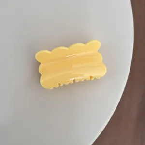 Gros plan détaillé d'une pince à cheveux jaune vif à bord ondulé, design élégant et simple.