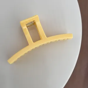 Gros plan d'une pince à cheveux rectangulaire jaune vif avec détail de ressort doré.
