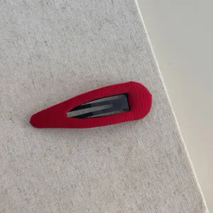 Gedetailleerde close-up van een rode stoffen haarklem met zachte textuur en metalen basis.