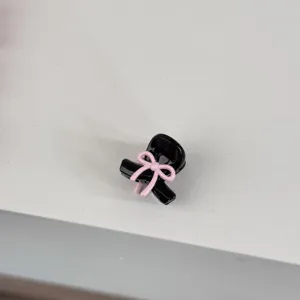 Close-up detail of a mini black hair claw clip featuring a cute pink bow, perfect for styling fringe.