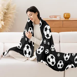 Cozy flannel blanket lifestyle detail showcasing black and white soccer pattern on white sofa.