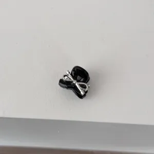 Detailed close-up of a mini black hair claw clip with a stylish silver bow decoration.