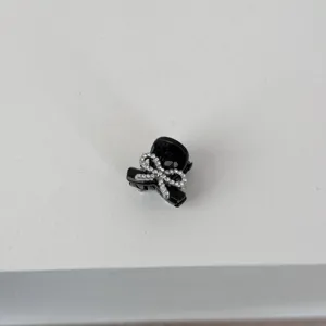 Close-up of a mini black hair claw clip adorned with a sparkling rhinestone bow detail.