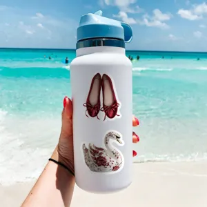 Water bottle detail showing decorative red ballet flats and swan stickers on beach background.