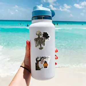 Bottiglia termica bianca con adesivi di Halloween, mostrata in dettaglio sulla spiaggia.