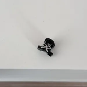 Detail shot of a cute black mini hair claw clip featuring a delicate silver bow decoration.