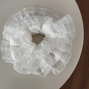 Detailansicht eines weißen Spitzen-Haargummis mit feiner Stofftextur und eleganten Lagen.