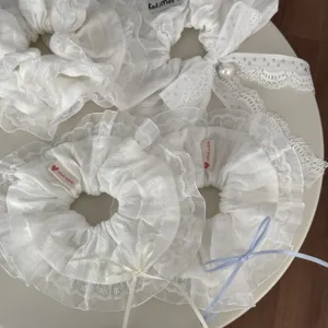 Detailansicht von weißen Haargummis aus Spitze mit eleganten Bändern und zarten handgemachten Details.