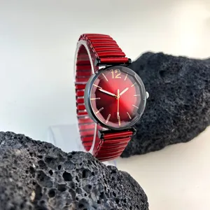 Detalle reloj cuarzo esfera roja, índices dorados, caja negra, correa elástica extensible.
