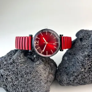 Primer plano de la esfera roja del reloj de mujer con correa metálica elástica y fina.